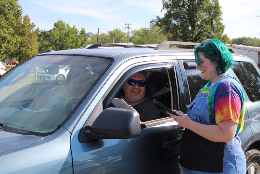 Outdoor photo of an SE Ohio Foodbank worker standing at a car window speaking to the person inside