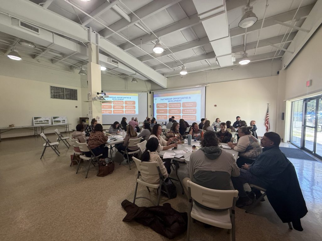 Photo of about 50 people from different orgs sitting around tables in the Glouster HAPCAP office to discuss Sunset Shelter partnership.