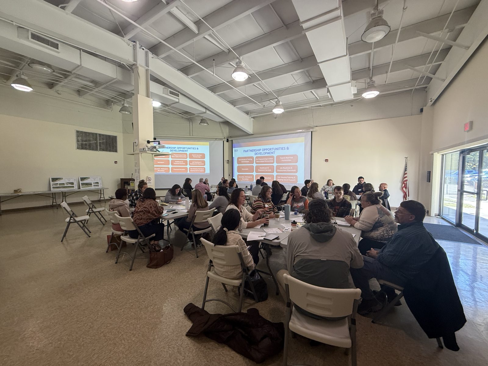 Photo of about 50 people from different orgs sitting around tables in the Glouster HAPCAP office to discuss Sunset Shelter partnership.
