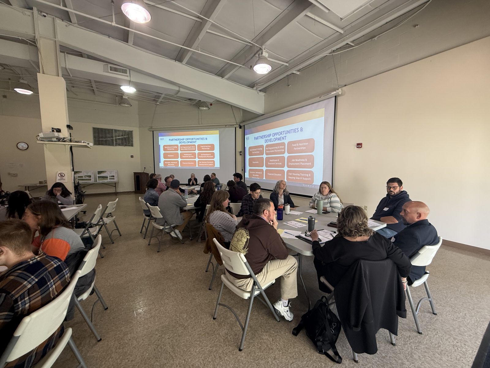Photo of about 50 people from different orgs sitting around tables in the Glouster HAPCAP office to discuss Sunset Shelter partnership.