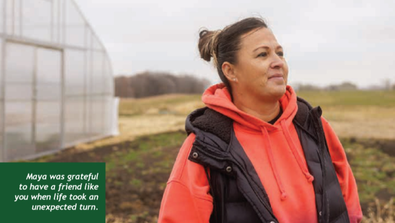 Photo of a woman standing in a field. She has brown hair and is in her 30s.