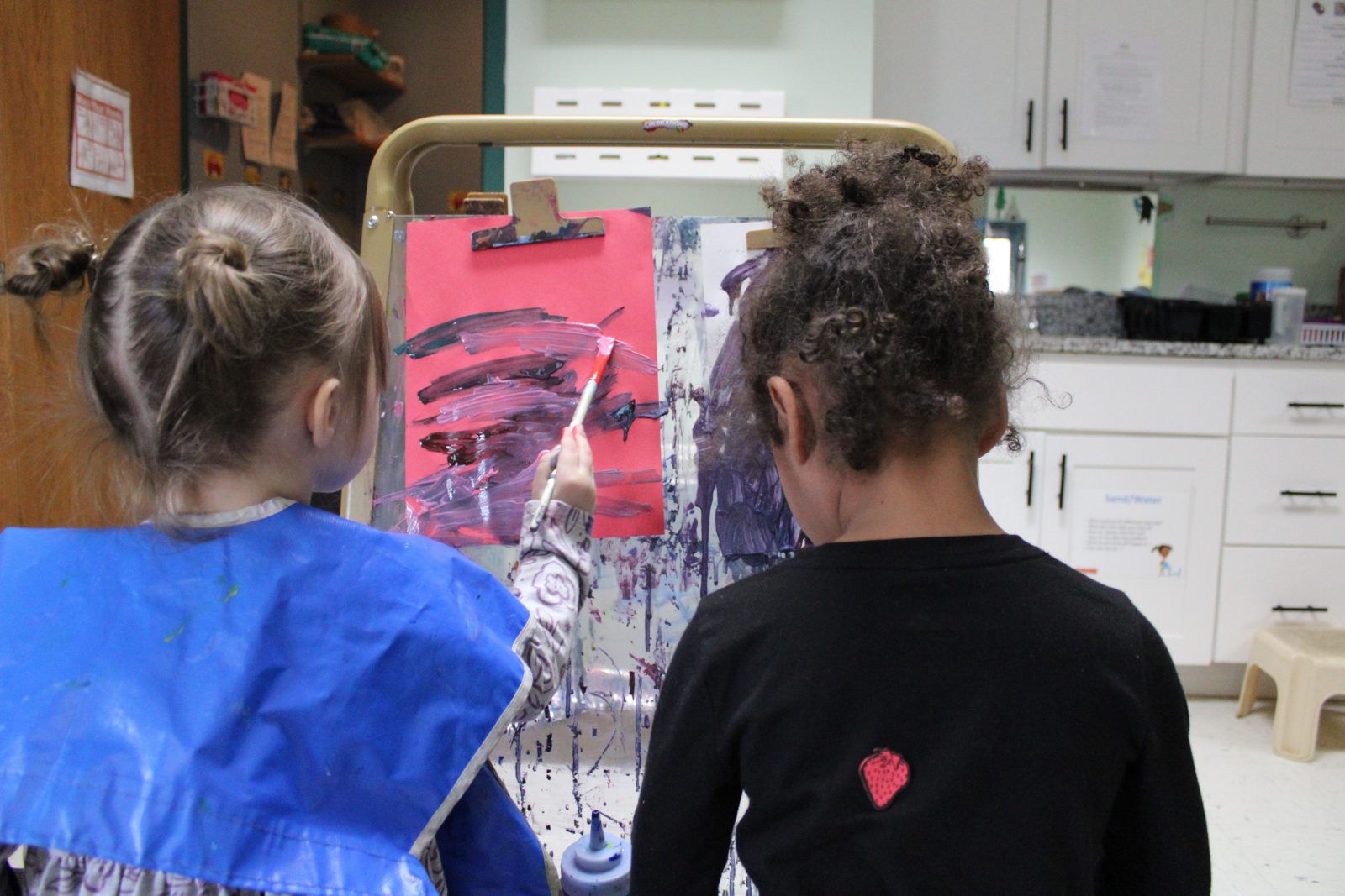 The back of two children painting on a canvas.
