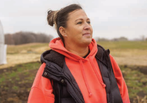 Photo of a woman standing in a field. She has brown hair and is in her 30s.